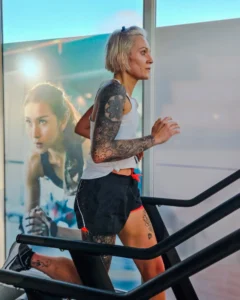 Femme tatouée courant sur un tapis de course.