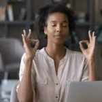 Femme méditant devant un ordinateur portable.