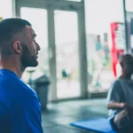 Homme en salle de gym écoutant un instructeur.